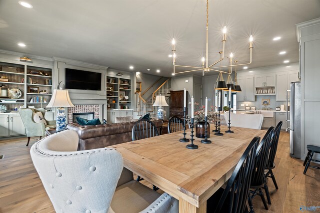 dining room with light hardwood / wood-style floors, a notable chandelier, a fireplace, and built in shelves