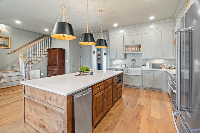 kitchen featuring hanging light fixtures, an island with sink, light hardwood / wood-style floors, appliances with stainless steel finishes, and backsplash