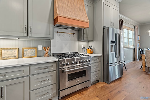 kitchen featuring custom exhaust hood, crown molding, light wood-type flooring, high quality appliances, and gray cabinetry