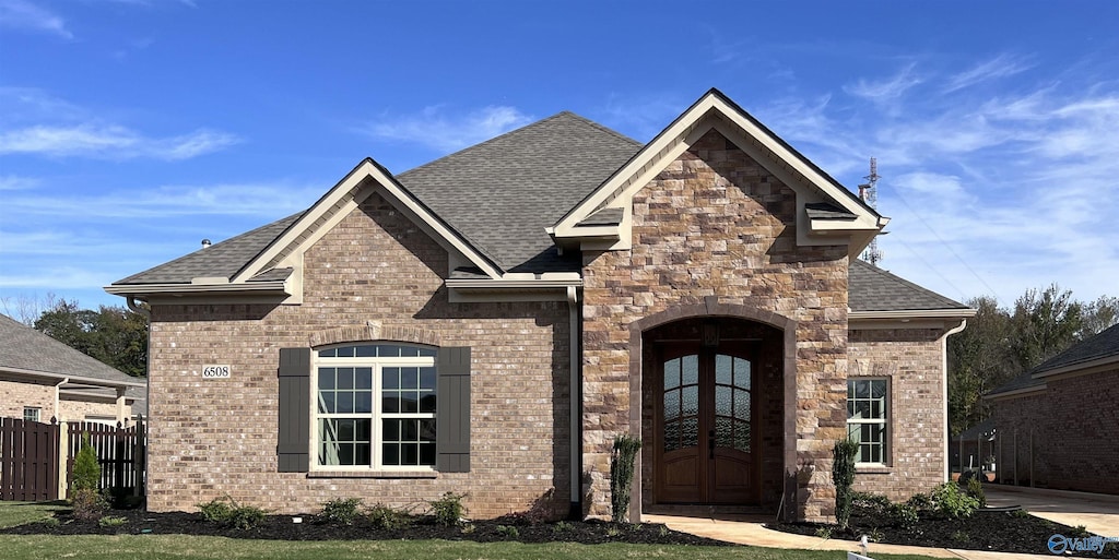 french country inspired facade featuring brick siding, roof with shingles, and fence