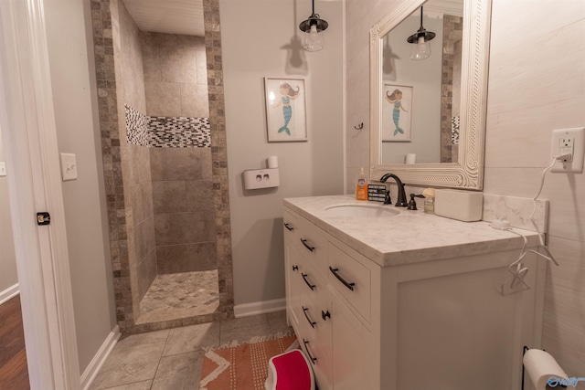 full bath with tiled shower, vanity, baseboards, and tile patterned floors