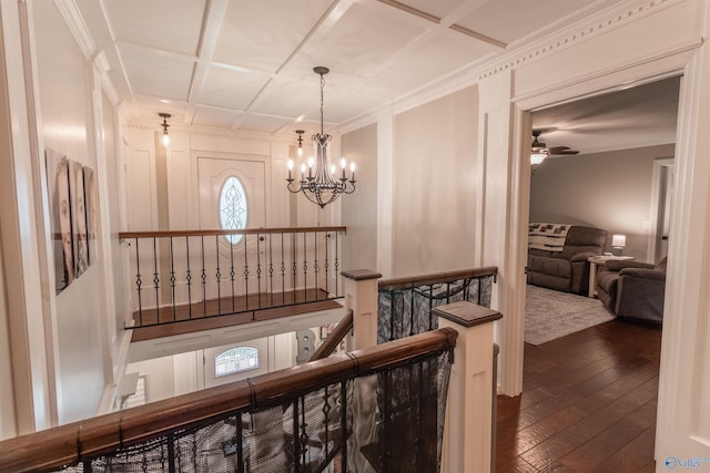 hall featuring dark wood-style flooring, crown molding, an inviting chandelier, an upstairs landing, and coffered ceiling