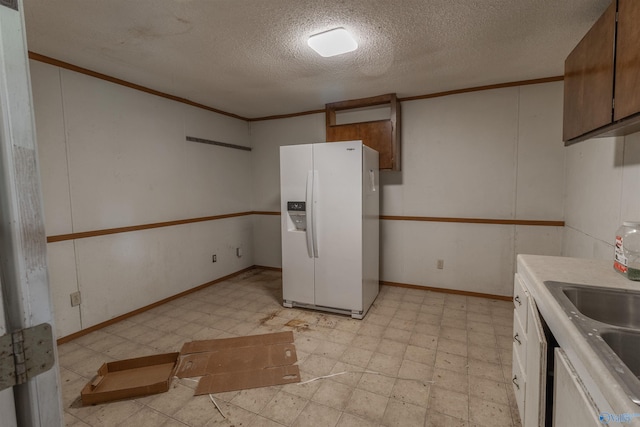 kitchen with ornamental molding, white refrigerator with ice dispenser, a textured ceiling, and light tile patterned floors