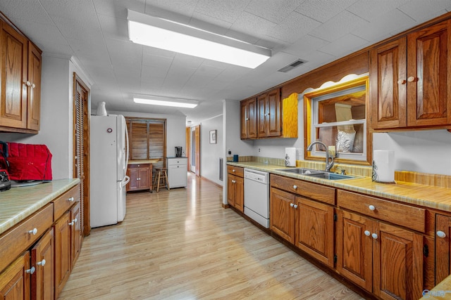 kitchen with a sink, visible vents, light wood finished floors, white appliances, and brown cabinetry