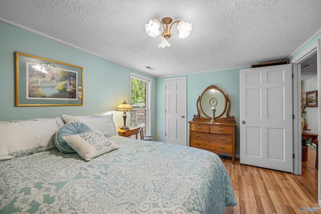 bedroom featuring a closet, visible vents, ornamental molding, a textured ceiling, and wood finished floors