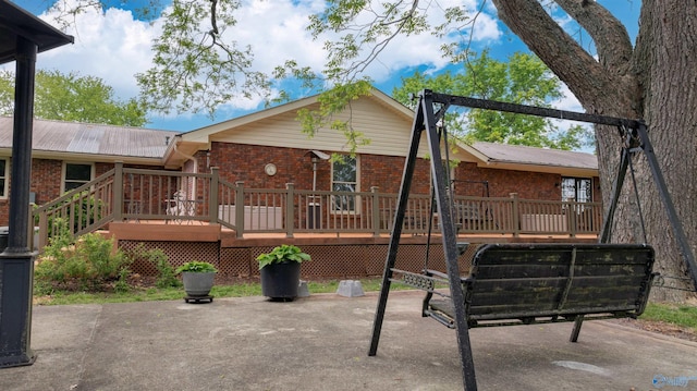 rear view of property featuring a wooden deck, a patio area, brick siding, and metal roof