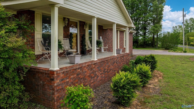 view of side of property featuring a lawn, covered porch, and brick siding