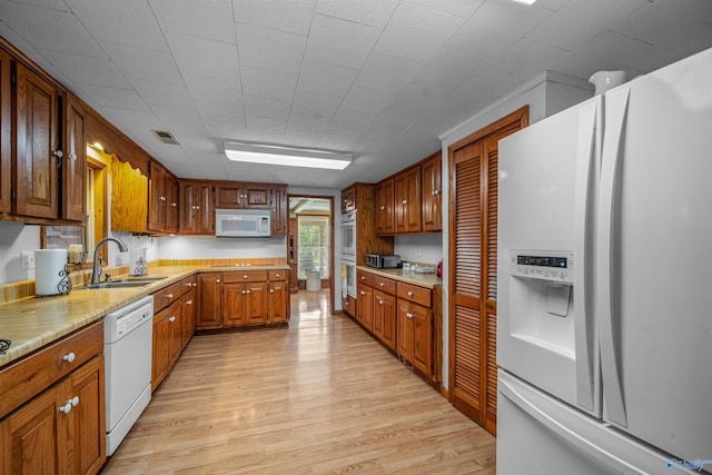 kitchen with brown cabinets, a sink, light wood-style floors, white appliances, and light countertops