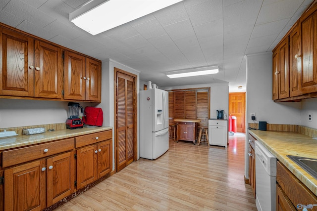 kitchen with brown cabinetry, white appliances, and light wood finished floors
