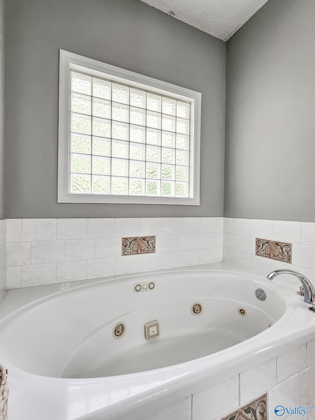 bathroom featuring plenty of natural light, a relaxing tiled tub, and a textured ceiling