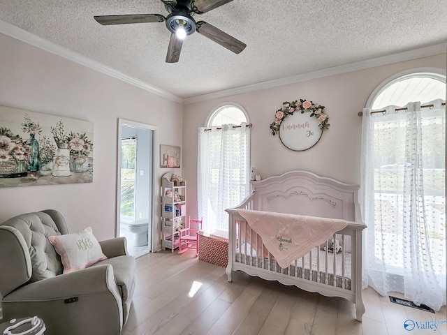 bedroom with crown molding, light hardwood / wood-style flooring, ceiling fan, a textured ceiling, and a nursery area