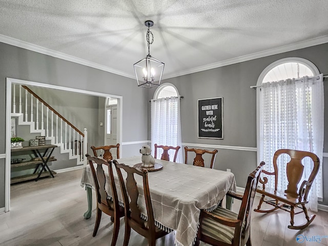 dining area with a textured ceiling, light wood-type flooring, ornamental molding, and an inviting chandelier