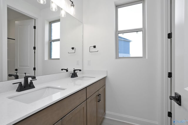 full bathroom with double vanity, baseboards, and a sink