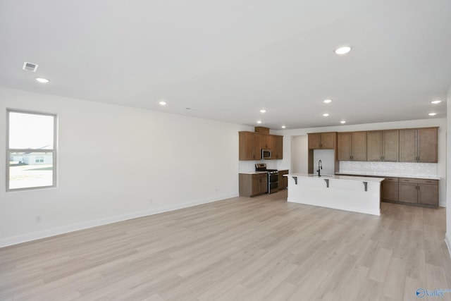 kitchen featuring visible vents, an island with sink, light wood-style floors, appliances with stainless steel finishes, and decorative backsplash