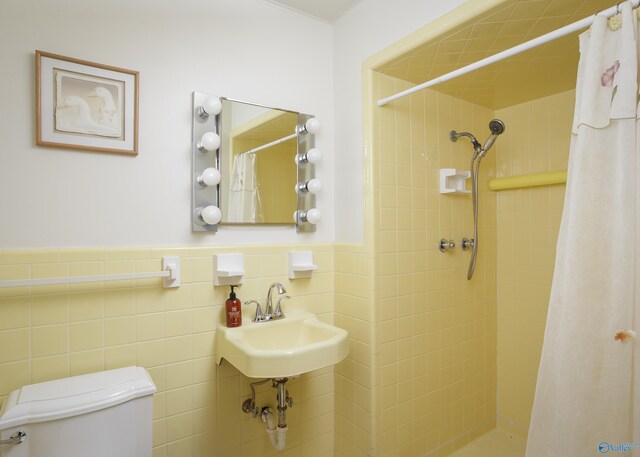 full bathroom featuring toilet, a wainscoted wall, a sink, tile walls, and tiled shower