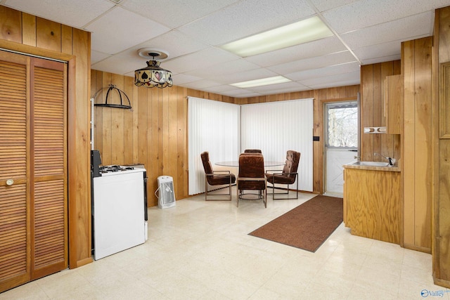 dining area with light floors, a drop ceiling, and wood walls