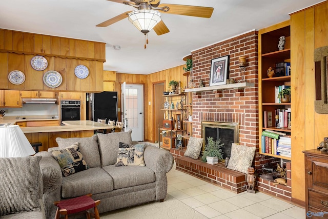 living room featuring a brick fireplace, light tile patterned flooring, a ceiling fan, and wood walls