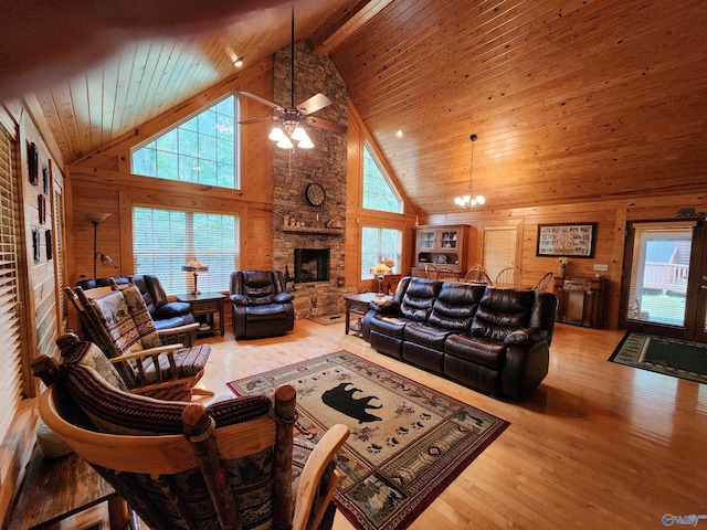 living room with a fireplace, wooden walls, light hardwood / wood-style flooring, ceiling fan with notable chandelier, and high vaulted ceiling