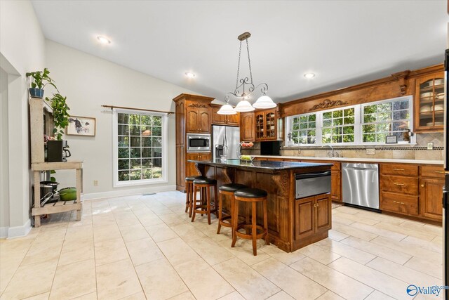 kitchen featuring vaulted ceiling, pendant lighting, tasteful backsplash, a kitchen island with sink, and double oven