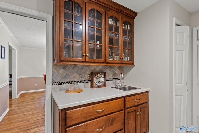 kitchen with tasteful backsplash, glass insert cabinets, brown cabinets, and a sink