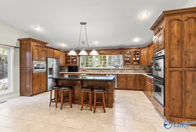 kitchen featuring stainless steel appliances, brown cabinets, glass insert cabinets, and a breakfast bar area