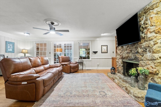 living room featuring a textured ceiling, ceiling fan, a fireplace, and wood finished floors