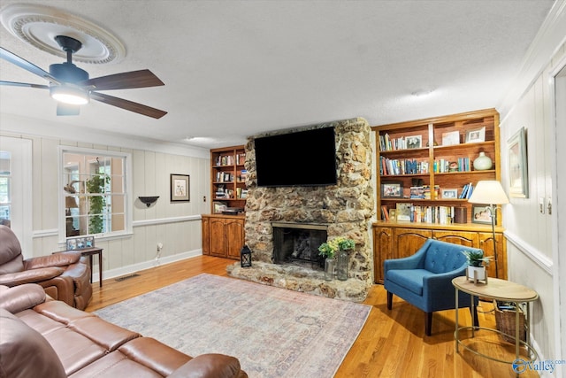 living room with ceiling fan, light hardwood / wood-style floors, a textured ceiling, and a stone fireplace