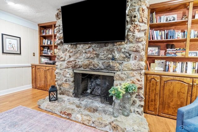 living room with ornamental molding, light hardwood / wood-style floors, a textured ceiling, and a stone fireplace