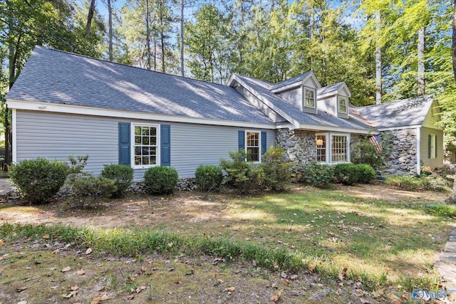 cape cod house with stone siding, a shingled roof, and a front yard