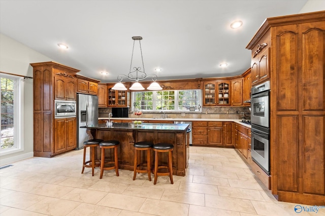 kitchen featuring appliances with stainless steel finishes, brown cabinets, glass insert cabinets, and backsplash