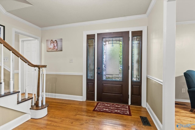 foyer entrance featuring wood finished floors, visible vents, baseboards, ornamental molding, and stairway