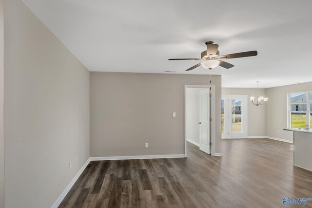 empty room featuring dark wood-type flooring, ceiling fan with notable chandelier, and baseboards