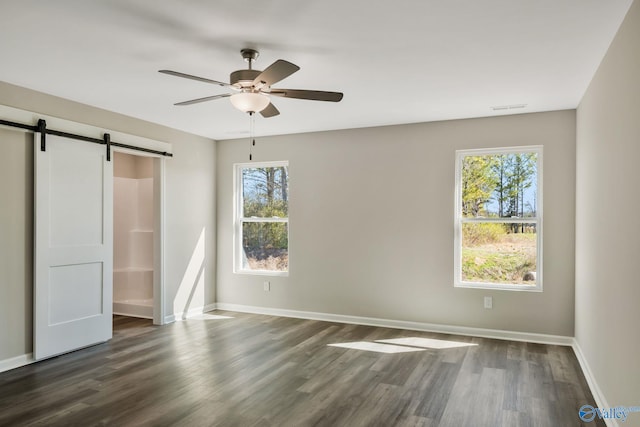 unfurnished bedroom featuring dark wood finished floors, a barn door, and baseboards