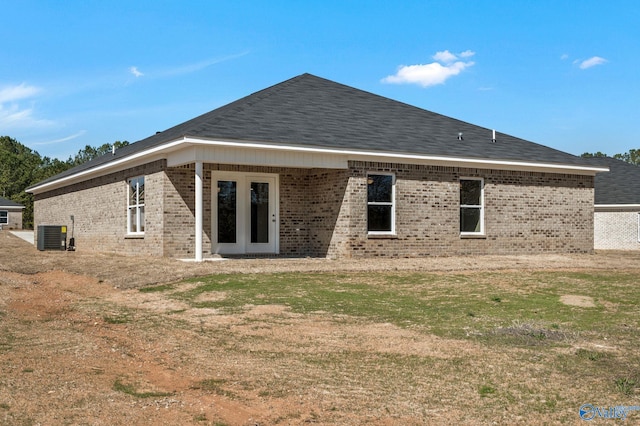 rear view of property with brick siding, central AC unit, a lawn, and a shingled roof