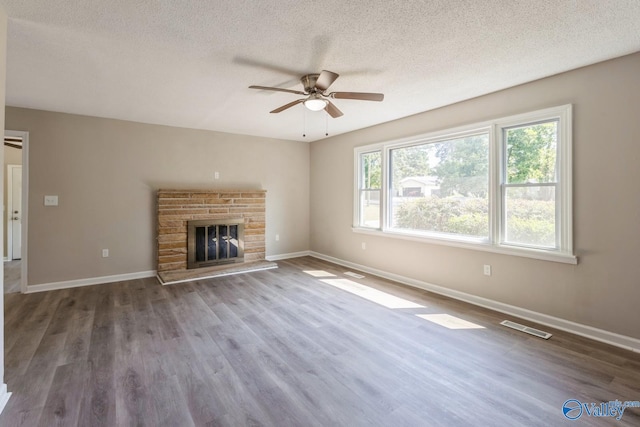 unfurnished living room featuring hardwood / wood-style floors, ceiling fan, a stone fireplace, and a textured ceiling