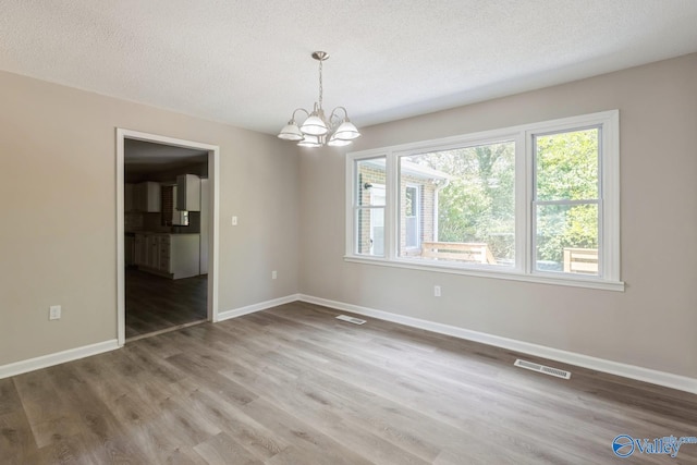 spare room featuring hardwood / wood-style floors, a textured ceiling, and an inviting chandelier