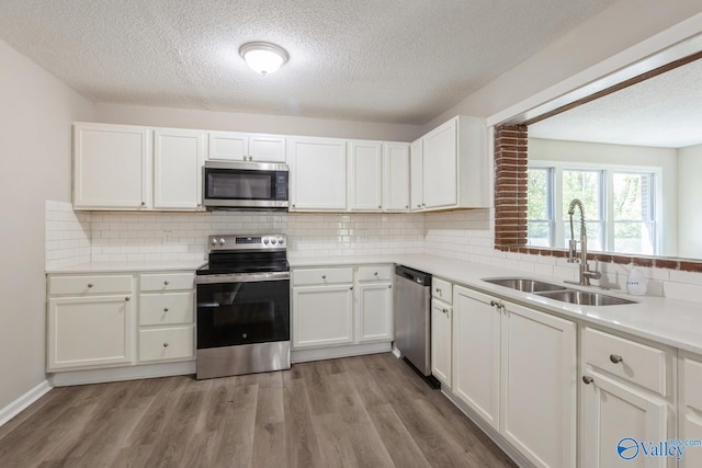 kitchen with white cabinets, sink, appliances with stainless steel finishes, tasteful backsplash, and light hardwood / wood-style floors