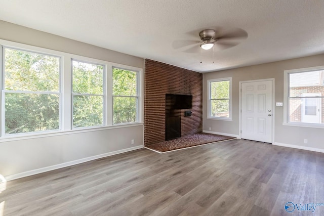 unfurnished living room featuring ceiling fan, a fireplace, light hardwood / wood-style floors, and a textured ceiling