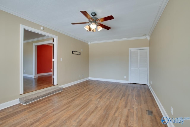 spare room with visible vents, wood finished floors, crown molding, baseboards, and ceiling fan