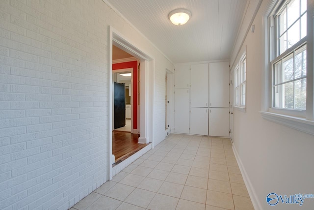 hallway featuring crown molding, light tile patterned flooring, baseboards, and brick wall