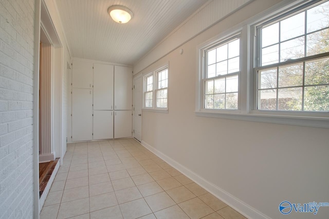 unfurnished room featuring light tile patterned flooring, baseboards, and brick wall