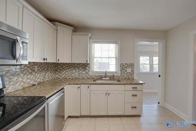 kitchen with light tile patterned flooring, a sink, stainless steel appliances, white cabinetry, and backsplash