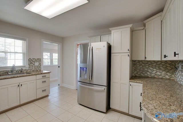 kitchen featuring tasteful backsplash, light stone countertops, light tile patterned floors, stainless steel fridge, and a sink