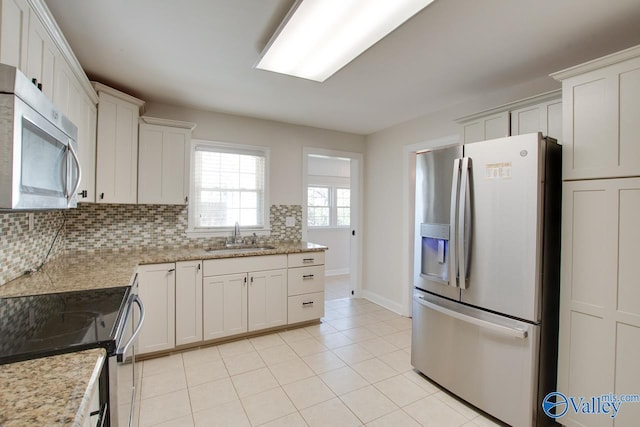 kitchen with backsplash, appliances with stainless steel finishes, light tile patterned flooring, white cabinets, and a sink