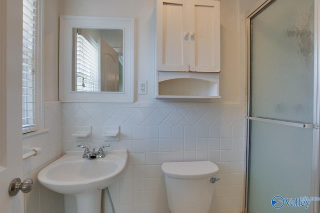 full bathroom with a wainscoted wall, toilet, a sink, a shower with door, and tile walls