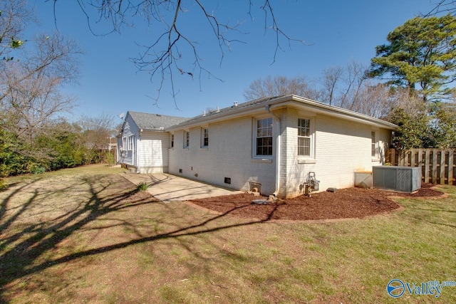 back of house with brick siding, fence, a patio area, a lawn, and crawl space