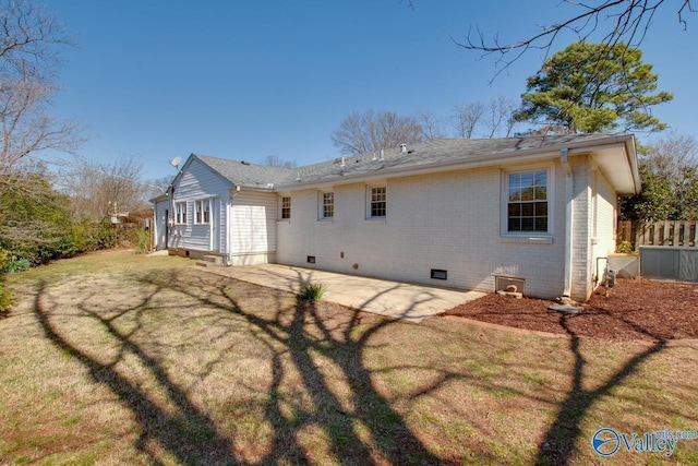 rear view of property featuring brick siding, fence, a patio area, a yard, and crawl space