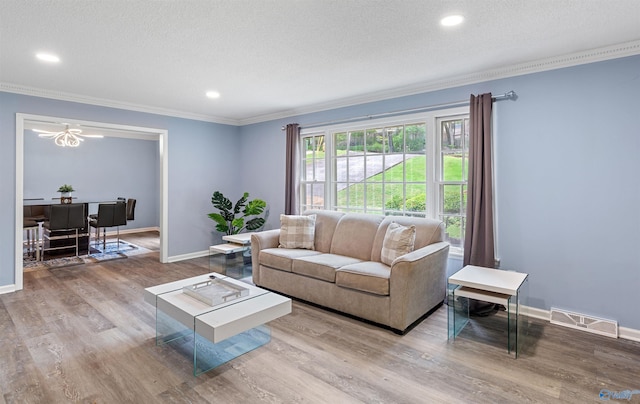 living room with wood finished floors, visible vents, baseboards, ornamental molding, and a textured ceiling