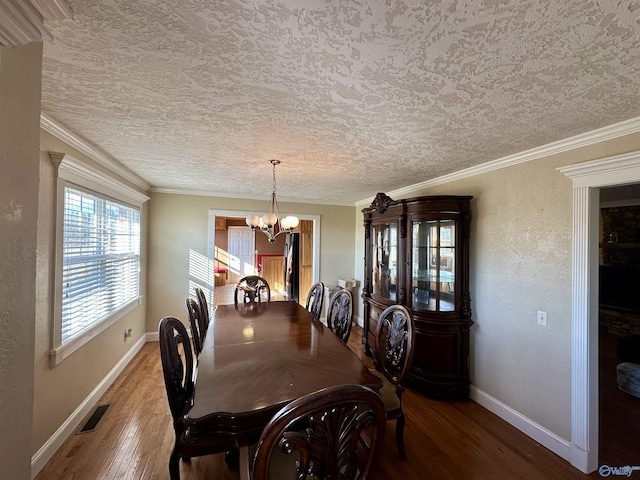 dining space featuring wood-type flooring, a textured ceiling, ornamental molding, and a notable chandelier