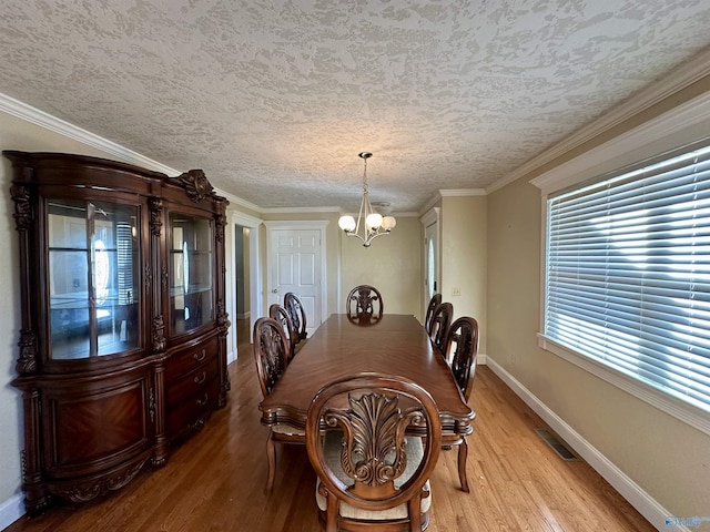 dining space featuring a textured ceiling, light wood-type flooring, ornamental molding, and an inviting chandelier